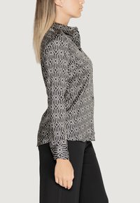 Camicia a maniche lunghe a righe bianche e nere con colletto, caratterizzata da disegni geometrici e una vestibilità leggermente affusolata. Tessuto dalla consistenza liscia.