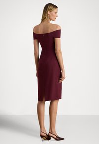 Bordové šaty s odhalenými ramenami, úzkym strihom, dĺžkou po kolená, detailmi textúry a rozparkom na chrbte. Nosia sa s hnedými sandálmi na opätku.