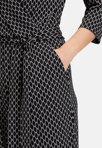 Svartvit mönstrad klänning med diamantvågmönster, midjeband, långa ärmar och sidoficka. Mjuk tygstruktur.