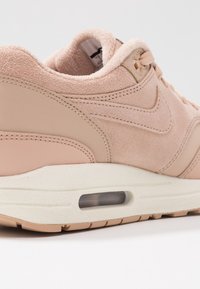 Světle růžová sportovní obuv z semišové a syntetické kůže, vybavená polstrovanou podrážkou a viditelnou vzduchovou jednotkou, zaobleným designem a prošívanými detaily.