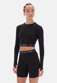 Juodas ilgomis rankovėmis trumpas švarkas ir prigludę šortai. Medžiaga atrodo lygi ir elastinga. Juostos turi „TED BAKER SPORT“ prekės ženklo ženklą.