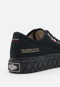 Sneaker noire en toile avec une semelle en caoutchouc texturée, dotée d'accents de couture multicolores et d'un logo doré en relief au niveau du talon.