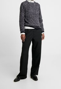 Marinblått texturerat stickat tröja med vita detaljer, svarta skräddade byxor och svarta loafers. Tröjan har ribbade muddar och nederkant.