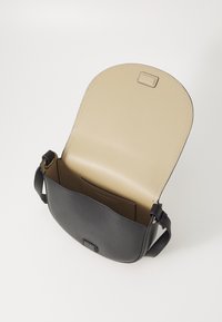 Czarna skórzana torebka o zakrzywionym kształcie, beżowe wnętrze i regulowany pasek. Ma przednią kieszeń i subtelne przeszycia.