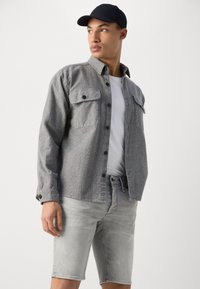 Gray button-up shirt with two chest pockets, paired with light gray denim shorts. Also features a plain white T-shirt and a black cap.