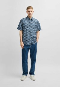 Kortarmige overhemd in blauw met een contrasterend geometrisch patroon, gecombineerd met rechtvallende denim jeans en witte sneakers.