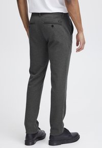 Men's grey tailored pants featuring a smooth texture, straight cut, side pockets, and a rear pocket with a button closure. Black shoes visible.