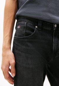Svart denimjeans med slim fit, med en liten rød, hvit og blå logo på framlommen og sølvfarget detaljer.