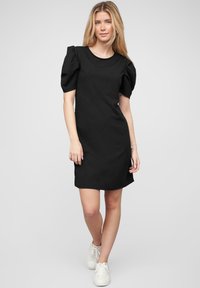 Robe noire en tissu lisse, avec des manches bouffantes courtes et un col rond. Design simple avec une coupe droite et une finition au niveau des genoux.