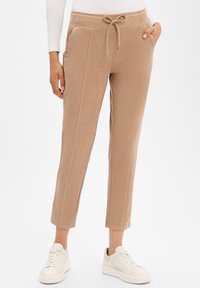 Beige jogger pants made of soft material, featuring a drawstring waist, side pockets, and tapered cuffs. Worn with white sneakers.