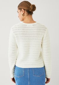 Maglione bianco lavorato a maglia con un motivo testurizzato, scollatura rotonda e maniche lunghe, abbinato a jeans blu chiaro.