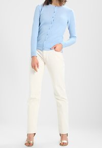 Cárdigan de punto azul claro con botones en la parte delantera, combinado con pantalones de pierna recta color crema y sandalias de tacón metálicas. Diseño sencillo.