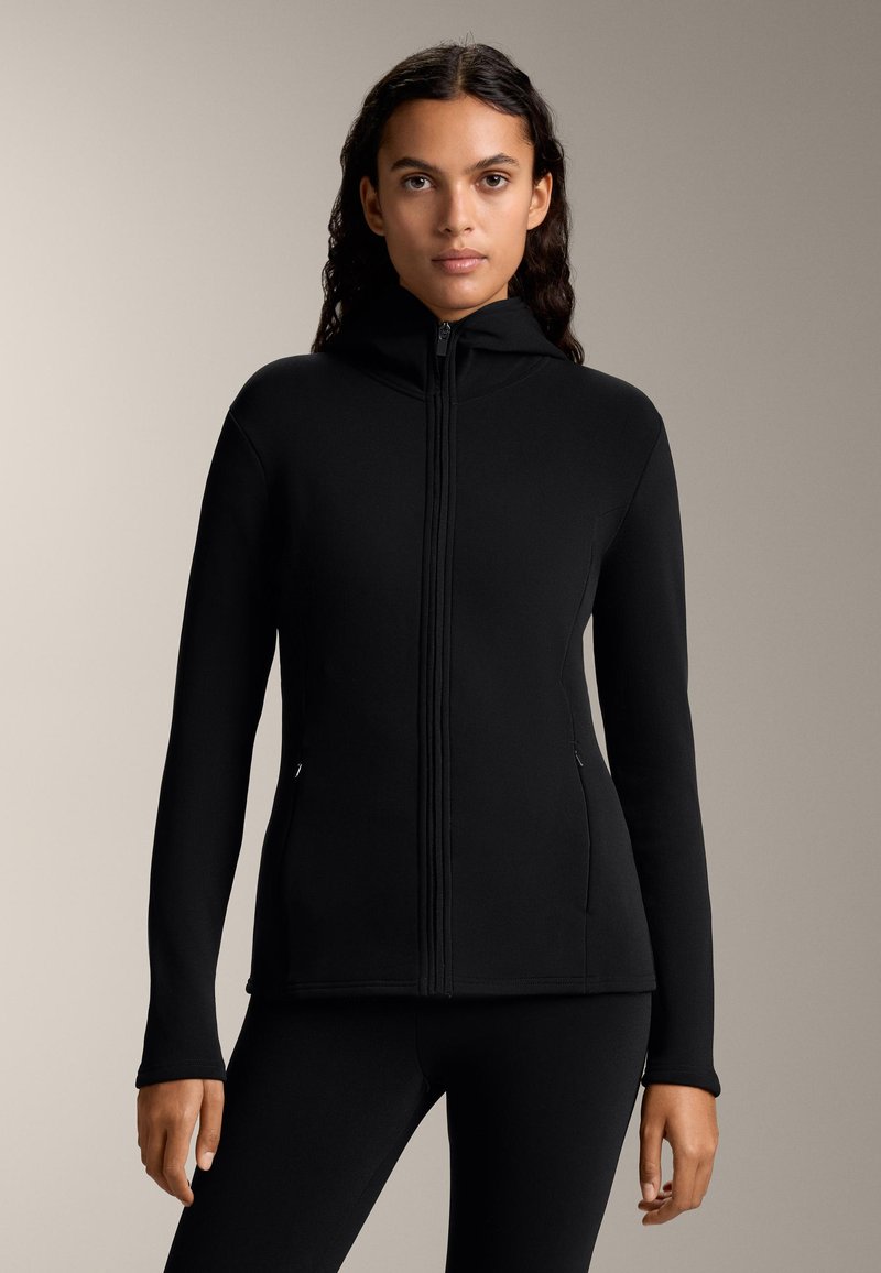 Črna zip-up kapuca z visokim ovratnikom, dolgimi rokavi in stranskimi žepi. Narejena iz gladkega blaga z prilegajočo se zasnovo in šivnimi podrobnostmi.