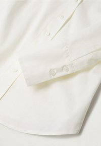 Chemise crème avec col italien, manches longues et poignets à boutons. Tissu de coton lisse avec fermeture classique à boutons sur le devant.