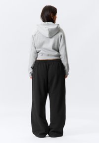 Ανοιχτό γκρι cropped φούτερ με κουκούλα και κορδόνι, σε συνδυασμό με μαύρο φαρδύ παντελόνι φόρμας ψηλόμεσο με ελαστική μέση.