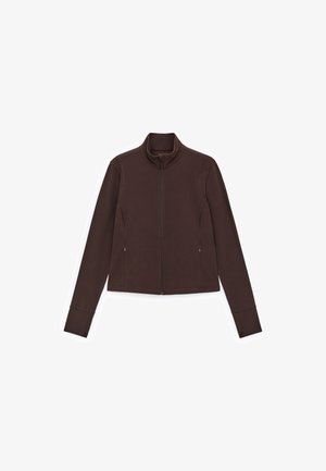 Bruine jas met rits, gemaakt van zachte stof, met een opstaande kraag, lange mouwen en zijzakken. Heeft gestikte details langs de naden.