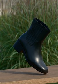 Black leather ankle boot with a sleek design, pointed toe, ribbed side detail, and a block heel resting on a wooden surface.