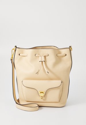 Beige leather bucket bag with a textured finish, drawstring closure, front pocket, and gold hardware accents. Adjustable shoulder strap included.