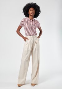 Camicia a maniche corte con un motivo geometrico in rosso, blu e bianco; abbinata a pantaloni beige a vita alta e a gamba larga. Scarpe testurizzate.