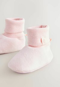 Chaussons de nuit roses avec un poignet élastique côtelé. Fabriqués en tissu doux et texturé. Présentent une petite étiquette en forme de fleur sur le côté.