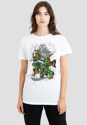 White cotton t-shirt featuring a graphic print of four green turtles in combat poses, with swords and other weapons, set against a cityscape background.