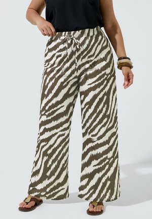 Kvinde iført løse, bredbenede bukser med zebra-tryk og snøre i taljen, sort ærmeløs top, armbånd og brune sandaler.
