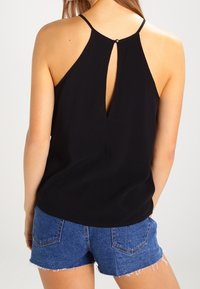 Černý bezramínkový top s výřezem na zádech, vyrobený z hladké látky. V kombinaci s džínovými šortkami s třepeným lemem a zadními kapsami.