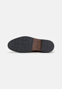 Black rubber sole with a textured grip pattern, contrasting brown leather accent, and embossed logo detail at the heel.