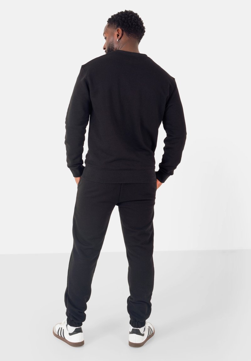 Felpa nera e pantaloni jogger realizzati in tessuto morbido, con polsini e vita a costine, abbinati a sneaker bianche con dettagli neri.