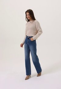 Μπεζ πλεκτό πουλόβερ με υφή, μπλε τζιν παντελόνι φαρδιάς γραμμής με ψηλή μέση και ταμπά ψηλοτάκουνα παπούτσια. Μινιμαλιστικό στυλ, ουδέτεροι τόνοι.