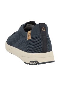 Baskets en maille bleu marine avec une finition texturée, accent en liège sur le talon et une semelle en caoutchouc beige portant le nom de la marque "SAOLA".