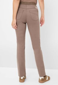 Brune strækbukser med en tætsiddende talje, glat tekstur, flagrende ben og baglommer. Sammen med casual sko med en hvid accent.