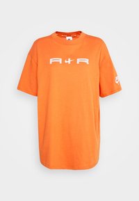 Orange bomulls t-shirt med rund hals, korta ärmar och fet vit text "A4R" på framsidan. Nike-logotyp på vänster ärm.