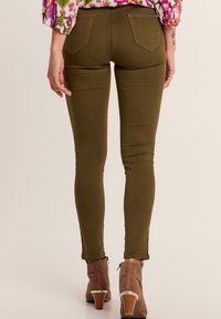 Jeans skinny verde oliva con una texture liscia, dotati di due tasche posteriori. Abbinati a stivaletti marroni.