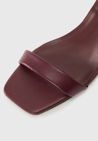 Bordo odinės slydimo šlepetės su plačiu dirželiu ir kvadratiniu pirštu. Dizainas minimalistinis, su glotnia, matinio paviršiaus tekstūra.