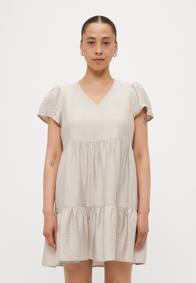 Ανοιχτό μπεζ φόρεμα με V λαιμόκοψη, κοντά φουσκωτά μανίκια και φούστα με επίπεδα και φαρδιά σχεδίαση που διαθέτει ρυτίδωση. Μινιμαλιστική σχεδίαση χωρίς μοτίβα.