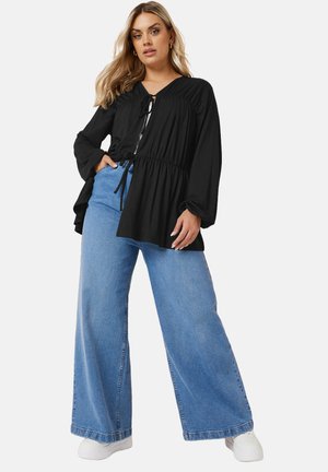 Black long-sleeve top with a gathered neckline and adjustable tie, paired with light blue wide-leg denim jeans and white sneakers.