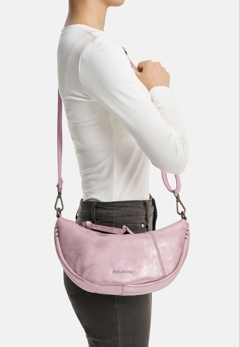 Sac à main en cuir rose avec une forme incurvée et une finition métallique. Doté d'une longue bandoulière et de détails de couture visibles, illustrant un design moderne.