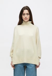 Kreminės spalvos golfas su laisvo silueto, reljefine tekstūra ir nuleistais pečiais, derinamas su šviesiai mėlynais plačiais džinsais.