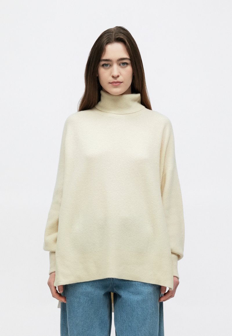 Kreminės spalvos golfas su laisvo silueto, reljefine tekstūra ir nuleistais pečiais, derinamas su šviesiai mėlynais plačiais džinsais.