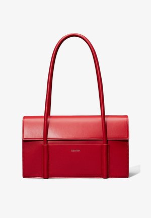 Sac à main en cuir rouge rectangulaire avec de longues anses arrondies et une poche avant, arborant un logo subtil Calvin Klein sur le panneau avant.