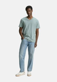 Ljust grön V-ringad t-shirt med korta ärmar, parat med ljusblå raka jeans och vita sneakers med bruna accenter.
