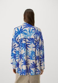 Lightweight, long-sleeve shirt featuring a blue tropical leaf print on a cream background. Relaxed fit with gathered detailing at the back.