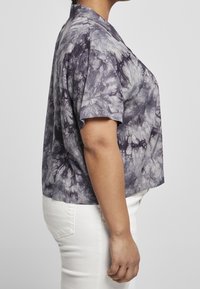 Camicetta a maniche corte con colletto in un motivo tie-dye viola, con una vestibilità rilassata, realizzata in tessuto leggero; abbinata a pantaloni bianchi.