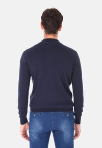 Maglione blu navy, design aderente, collo e polsi a coste, texture morbida, indossato con jeans azzurri chiari. La vista posteriore mostra dettagli minimi.