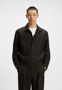 Dark brown, short jacket with a collared neckline, front pockets, and button closure. Made from textured fabric with a tailored fit.