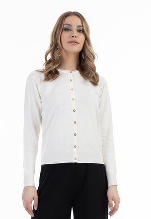 Cardigan alb din tricot cu mâneci lungi, decolteu rotund și închidere cu nasturi aurii. Textură moale cu margine ribbed, asociat cu pantaloni negri.