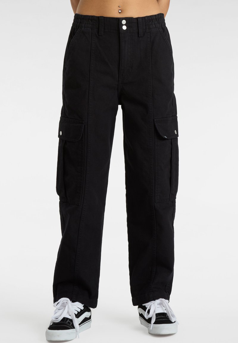 Zwarte cargobroek met een ontspannen pasvorm, voorzien van zijzakken, knoopaccenten en een elastische tailleband. Gecombineerd met zwart-witte sneakers.