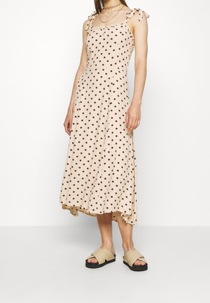 Robe midi beige à pois avec des bretelles ajustables et nouables, ourlet évasé et tissu léger. Associée à des sandales croisées beiges.