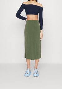 En off-shoulder marinblå långärmad topp parat med en knälång olivgrön kjol, kompletterad med ljusblå remmar på plattformssandaler.